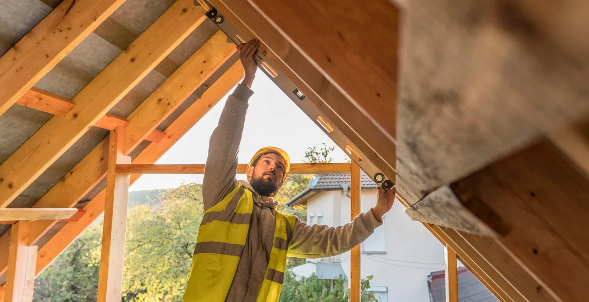 Photographie d'un chef de chantier Alternative Bois Concept qui inspecte une charpente à l'aide d'un niveau à bulle, afin d'en vérifier la bonne inclinaison de pente.